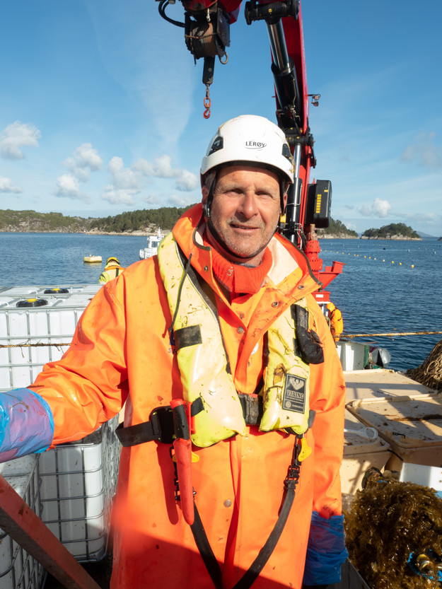 En mann med regnklær, hjelm og redningsvest på en båt