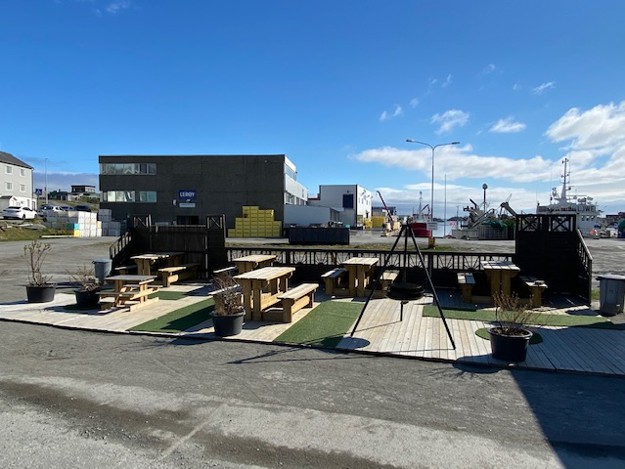 Park area with benches, a bonfire and green areas, in the back is a square factory with the Lerøy-logo.