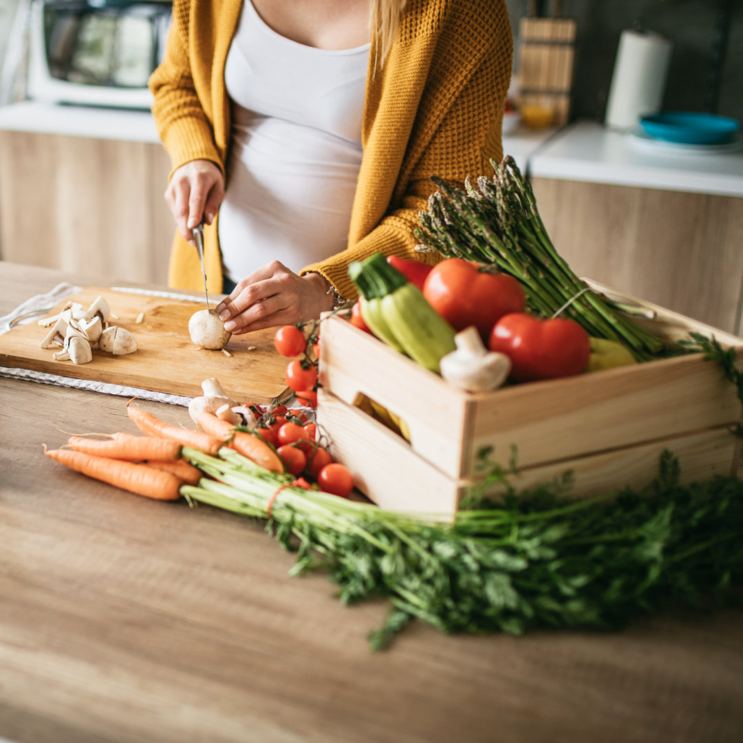 Gravid kvinne på kjøkkenet, skjærer grønnsaker 